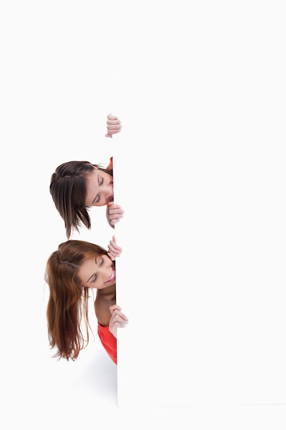 Teenagers hiding behind a blank poster while showing their heads on the side