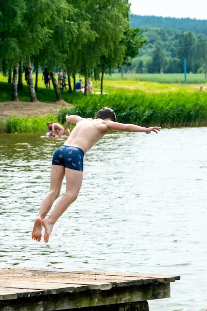십대들은 더운 여름날 물에 뛰어들어 호수에서 수영합니다 탁 트인 연못에서 활동적인 레크리에이션을 합니다 아이들은 물에 뛰어들어 곡예 묘기를 선보입니다