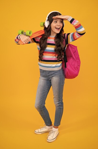 Teenagers lifestyle casual youth culture teen girl with skateboard and headphone over isolated yellow studio background cool modern teenager in stylish clothes happy teenager