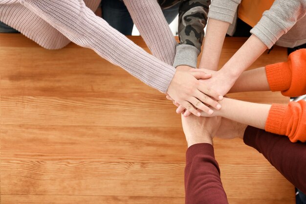 Photo teenagers putting hands together over table