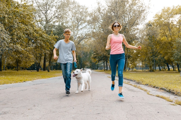 Teenagers running with white dog Husky on the road in the park