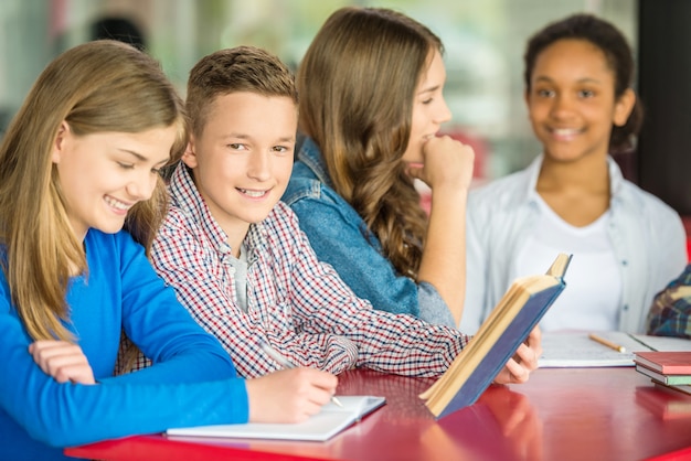 Photo teenagers sitting at table in cafe and doing homework.