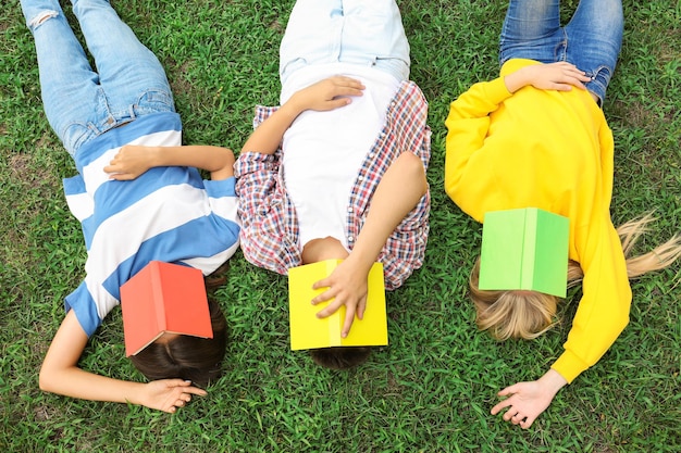 Teenagers with books lying on green grass