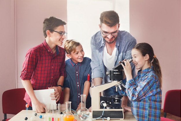 Teenagers with teacher making chemical experiment in laboratory with reagents and looking through a microscope. Early development, education, diy, innovation concept. Stem education.