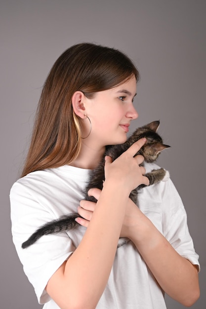 Teengirl holding a baby cat on gray background Portrait of young girl with kitten Kids and pets