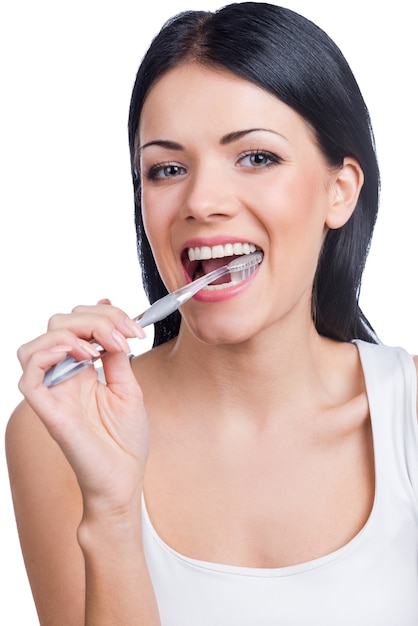 Teeth care. Portrait of beautiful young woman holding a toothbrush in her mouth and looking at camera while standing against white background