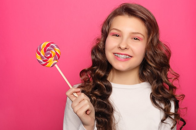 Teeth, emotions, health, people, dentist and lifestyle concept - Woman with dental braces holding lollipop. Healthy smile woman with clear brackets