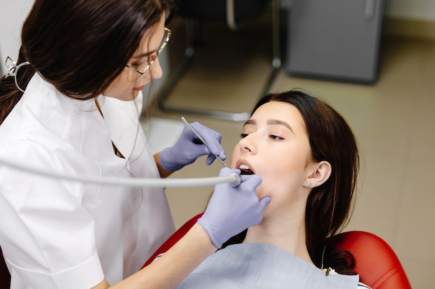 Teeth health concept Attractive girl opening mouth under treatment at dental clinic and dentist woman doing treatment her teeth