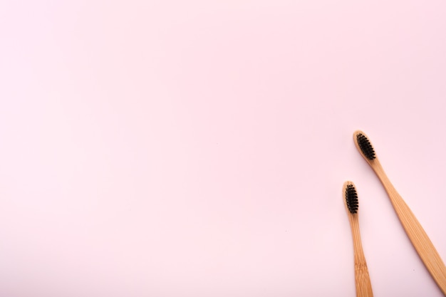 Teeth hygiene and oral dental care products on pink color background with copy space. Eco-friendly bamboo toothbrushes and cotton flowers. Flat lay, top view composition, mockup. Morning concept.