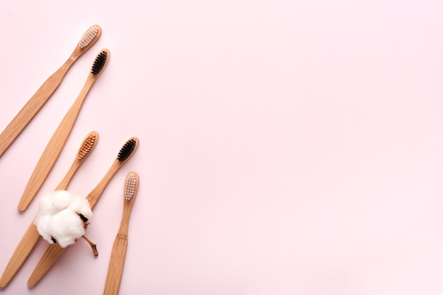 Teeth hygiene and oral dental care products on pink color background with copy space. Eco-friendly bamboo toothbrushes and cotton flowers. Flat lay, top view composition, mockup. Morning concept.