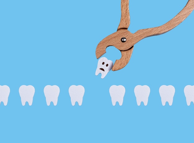 Teeth row and dental forceps Pulling bad sick tooth with sad emoji because of decay periodontal disease Oral health and dentist work concept on blue background Children game at doctor