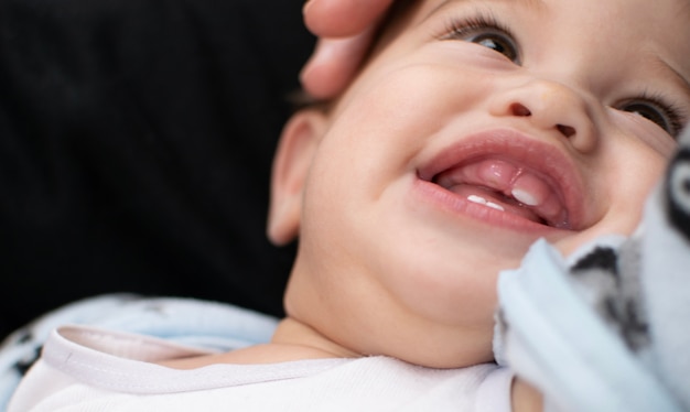 Teething baby has a big smile shows the gum and coming tooth