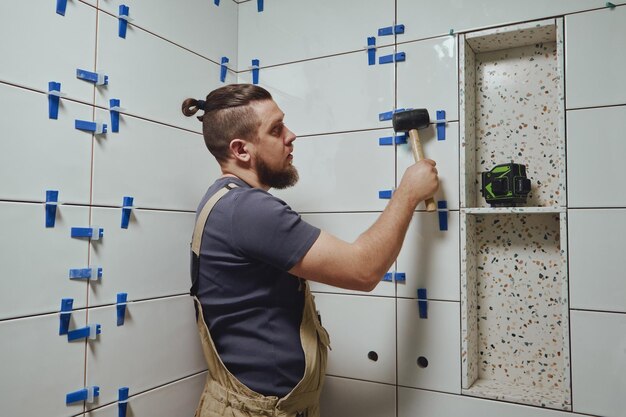 Tegelzetter slaat de wiggen van het nivelleersysteem voor keramische tegels van de muur in de badkamer