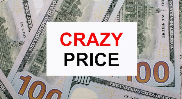 Tegen de achtergrond van Amerikaanse dollars een witte kaart met de tekst CRAZY PRICE. Financieel concept