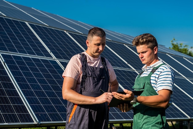 Tegen de achtergrond van zonnepanelen schrijven twee arbeiders in een tabletplan van het uitgevoerde werk