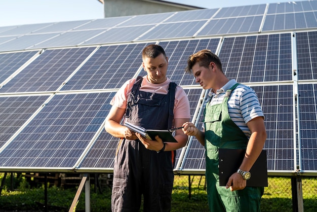 Tegen de achtergrond van zonnepanelen schrijven twee arbeiders in een tabletplan van het uitgevoerde werk