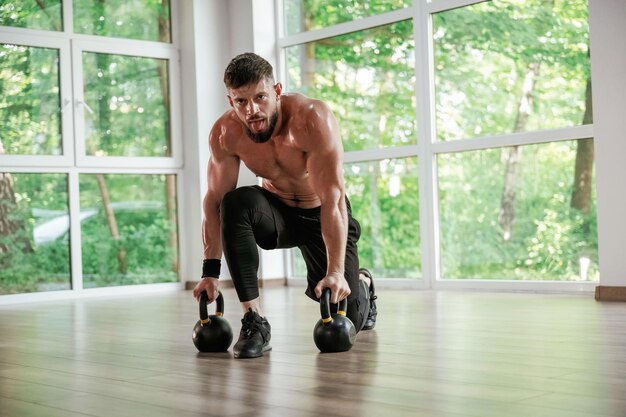Tegen de ramen met dumbbells Sterke gespierde man werkt uit in de sportschool