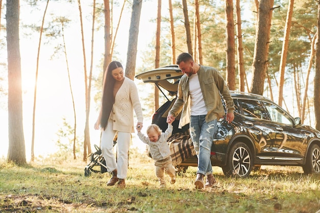 Tegen zwarte auto Gelukkige familie van vader, moeder en dochtertje is in het bos