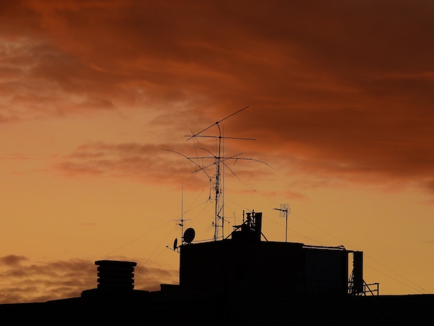 Tejados chimeneas y antenas de telecomunicaciones en contraste con el cielo anaranjado al anochecer