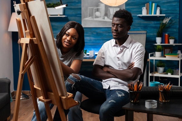 Tekening van een vrouwelijke leraar die toezicht houdt op kunstwerken van een Afro-Amerikaanse mannelijke student in het kunstklaslokaal. Vrienden leren samen de kunst van het schetsen met kleurpotloden in het moderne atelier thuis.