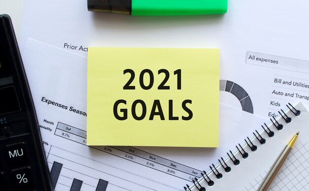 Tekst 2021 GOALS op de pagina van een notitieblok dat op financiële grafieken op het bureau ligt.