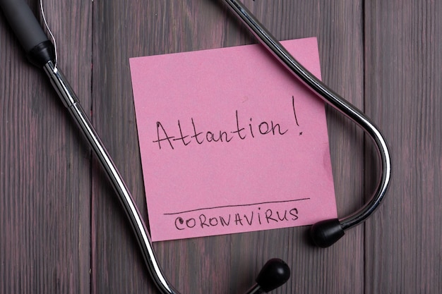 Foto tekst attantion coronavirus op notitie en stethoscoop op houten achtergrond