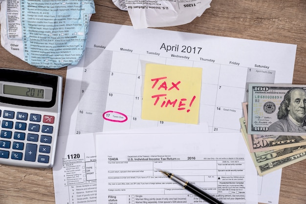 Tekst "belastingtijd" op belastingformulieren 1040 met pen, rekenmachine en geld.