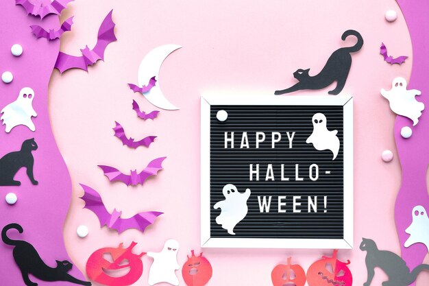 Tekst Happy Halloween op letterbord, letterbord. Leuke achtergrond met zwarte katten, levendige paarse papieren vleermuizen, roze pompoenen, witte geesten. Plat lag op roze en paars papier met witte maan.