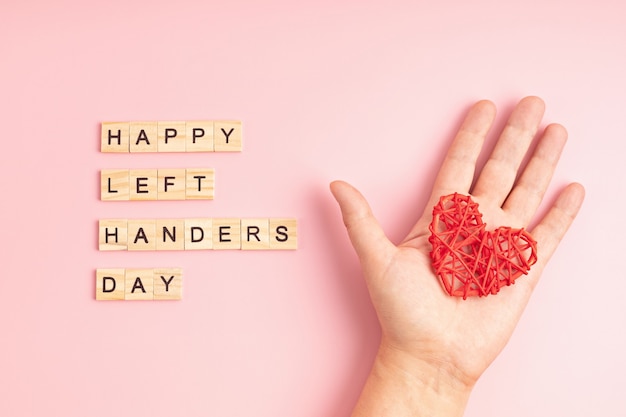 Tekst happy left handers day geschreven met houten letters en hart over roze achtergrond