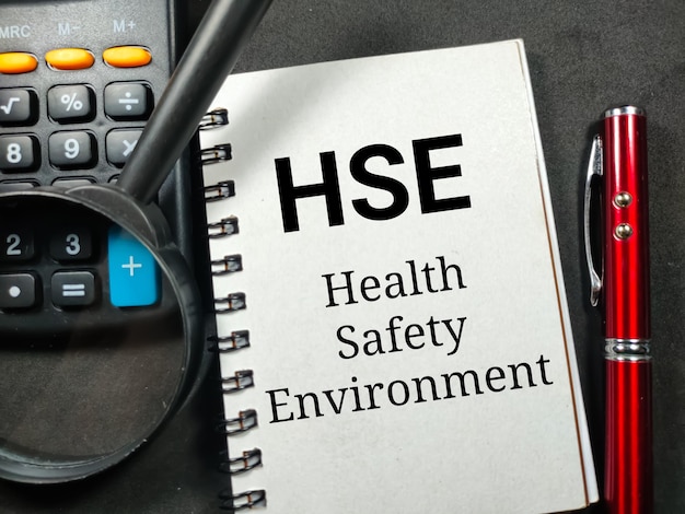 Tekst HSE Health Safety Enviroment schrijven op notebook met vergrootglas pen en rekenmachine