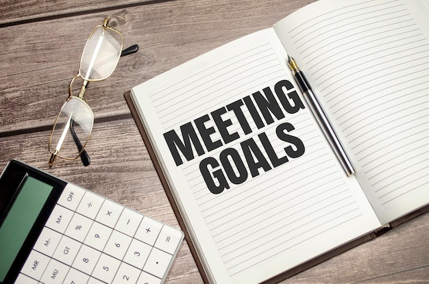 Tekst MEETING GOALS op bruin dagboek met rekenmachine bril op houten achtergrond