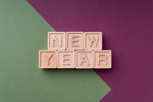 Foto tekst nieuwjaar gemaakt van houten kubussen op een papier heldere groene rode achtergrond close-up bovenaanzicht plat leggen kerst achtergrond voor ansichtkaart kerst lay-out gelukkig nieuwjaar