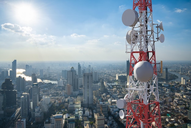 都市の背景に5Gセルラーネットワークアンテナを備えた通信塔