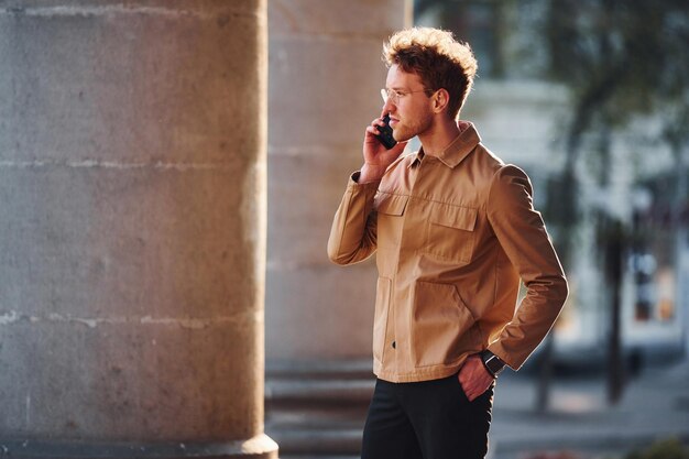 Telefonisch praten Elegante jonge man in formele stijlvolle kleding buiten in de stad