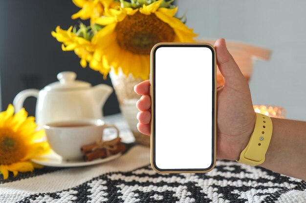 Telefoon in handen isoleren op de achtergrond van een kopje thee met zonnebloemen