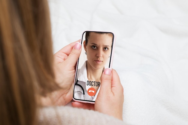 Telefoon in vrouwelijke handen in bed met doktersoproep Digitale gezondheidszorg en telegeneeskunde online concept