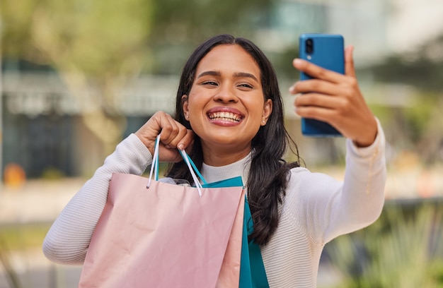 Telefoon selfie en winkelen met een vrouw in een stad met gelukkig ontspannen en lachende shopper met boodschappentassen Retail fashion en social media influencer die goed nieuws deelt, verkoop en korting online