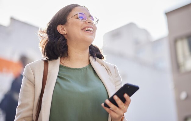 Telefoon wandelen en gelukkige vrouw buiten in een stad met communicatie-internetverbinding en app Lach professionele persoon en stedelijke weg met smartphone voor berichtenchat of sociale media op reis