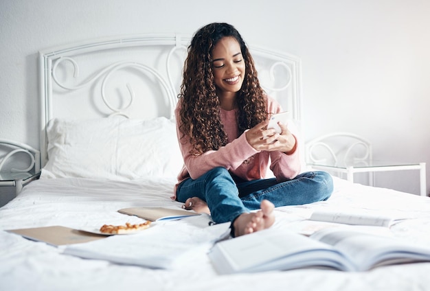 Telefoonboeken en ontspannen studente pauze van leren studeren en onderwijs examenpapier in bed Universiteit of universiteitsmeisje rusten met mobiele smartphone voor online sociale media en glimlachen op post