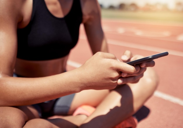 Foto telefoonfitness en vrouw op sociale media op een racecircuit om te zoeken naar hardlooptraining of trainingsinhoud online hands-netwerkapp en sportmeisje rustend op een pauze na het sporten om te ontspannen