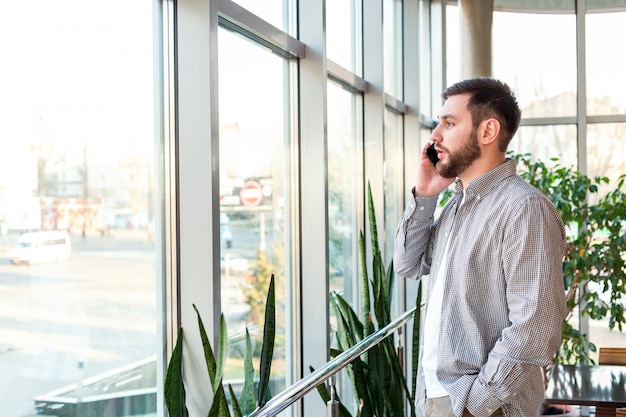 Telefoongesprek in stedelijke moderne kantoor. Slimme baard man onderhandelt door smartphone. Aantrekkelijke zakenman freelancer in café. Jonge Kaukasische succesvolle smartphone van de mensenholding voor het bedrijfswerk.