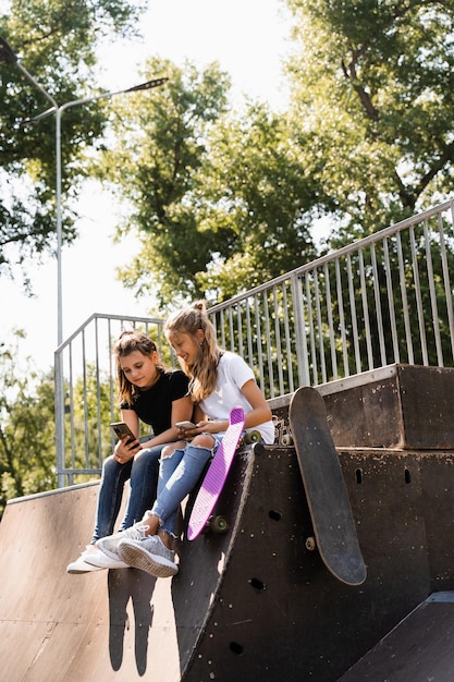 Telefoonverslaafde sportkinderen met skateboard en pennyboards gebruiken telefoons in plaats van skaten en spelen samen Kinderen kijken naar smartphones op sporthelling Kinderen verslaving aan telefoons