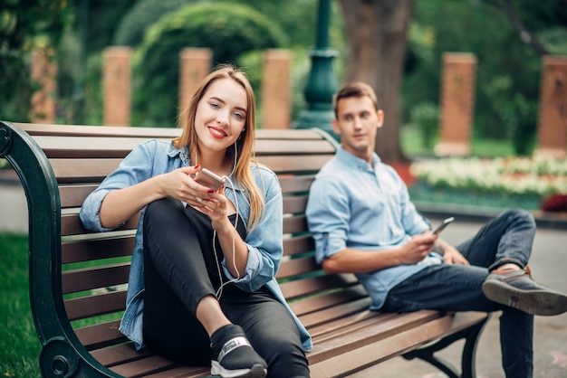 Telefoonverslaving, paar negeren elkaar op de bank in het park. Man en vrouw die hun smartphones gebruiken, sociaal verslaafde mensen