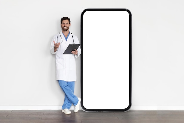 Telehealth Concept Handsome Male Doctor In Uniform Standing Near Big Blank Smartphone