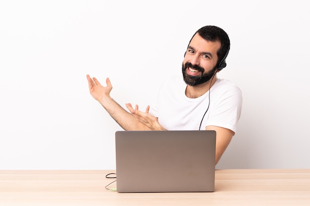 Telemarketeer blanke man aan het werk met een headset en met laptop die zijn handen naar de zijkant uitstrekt om uit te nodigen om te komen.