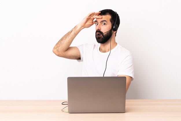 Telemarketeer blanke man aan het werk met een headset en met laptop doen verrassingsgebaar tijdens het kijken naar de zijkant