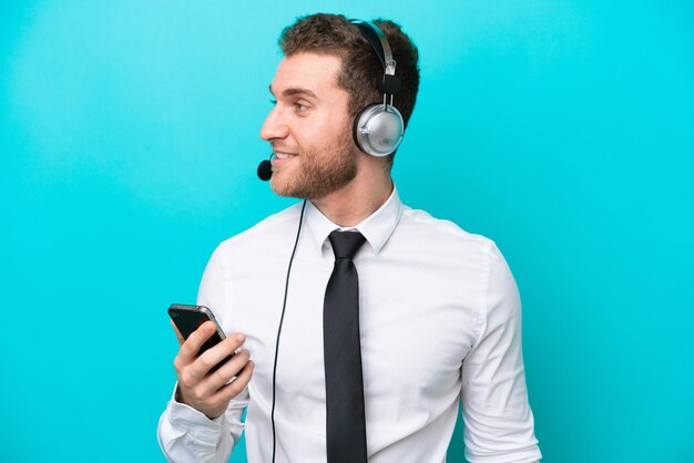 Telemarketeer blanke man aan het werk met een headset geïsoleerd op blauwe achtergrond een gesprek voeren met de mobiele telefoon met iemand