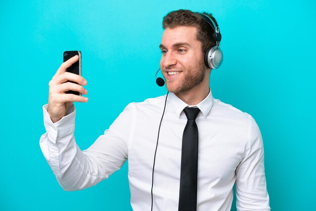 Telemarketeer blanke man aan het werk met een headset geïsoleerd op blauwe achtergrond maken een selfie