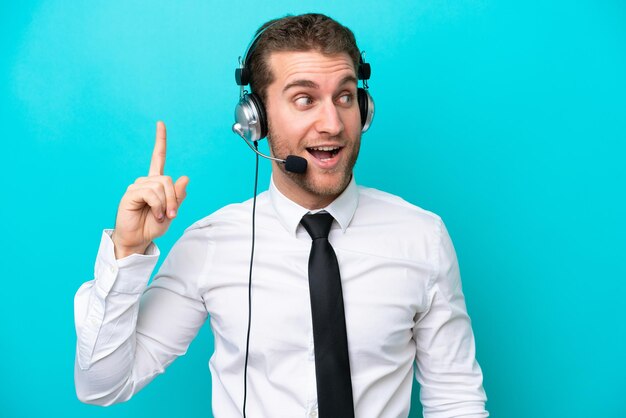 Telemarketeer blanke man aan het werk met een headset geïsoleerd op blauwe achtergrond met de bedoeling de oplossing te realiseren terwijl hij een vinger optilt