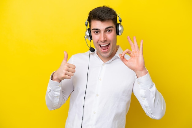 Telemarketeer blanke man aan het werk met een headset geïsoleerd op gele achtergrond met ok teken en duim omhoog gebaar